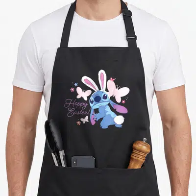 Hoppy stitch apron - Blue Stitch wearing bunny ears with pink butterflies and purple Hoppy Easter text — shown on a black cotton canvas apron against a white background