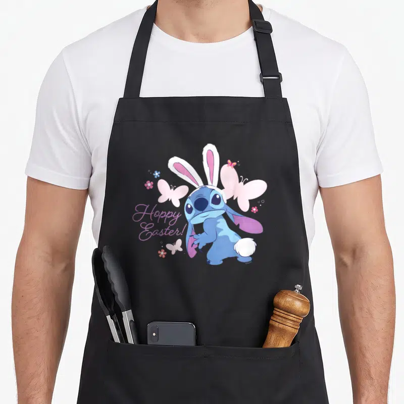 Hoppy stitch apron - Blue Stitch wearing bunny ears with pink butterflies and purple Hoppy Easter text — shown on a black cotton canvas apron against a white background