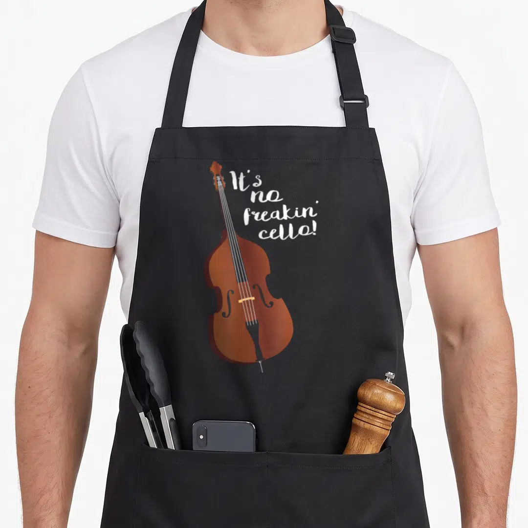 Double joke apron - Brown cartoon double bass next to white stacked text reading It's no freakin' cello! — shown on a black cotton canvas apron against a white background
