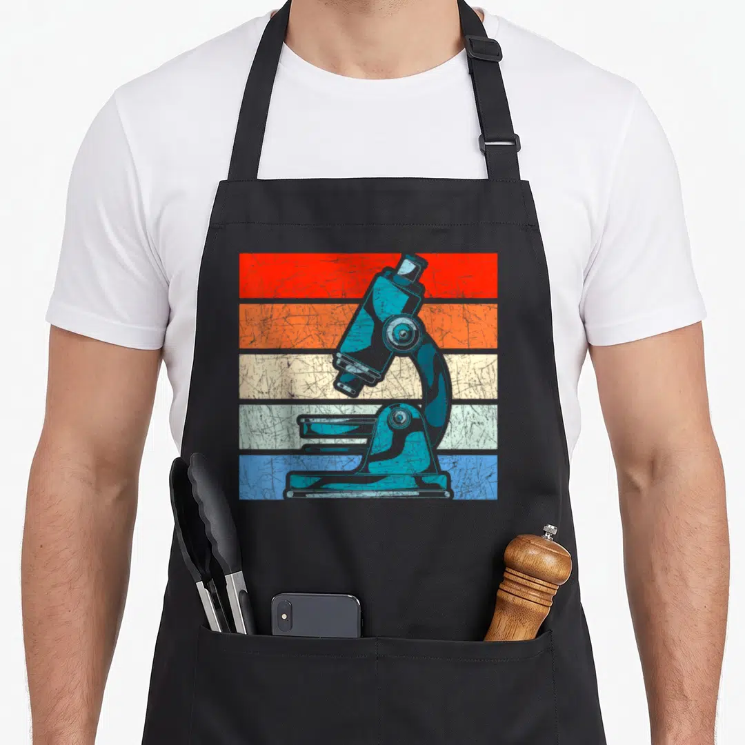 Microscope laboratory apron - Blue microscope centered on five horizontal stripes in red, orange, beige, light blue — shown on a black cotton canvas apron against a white background