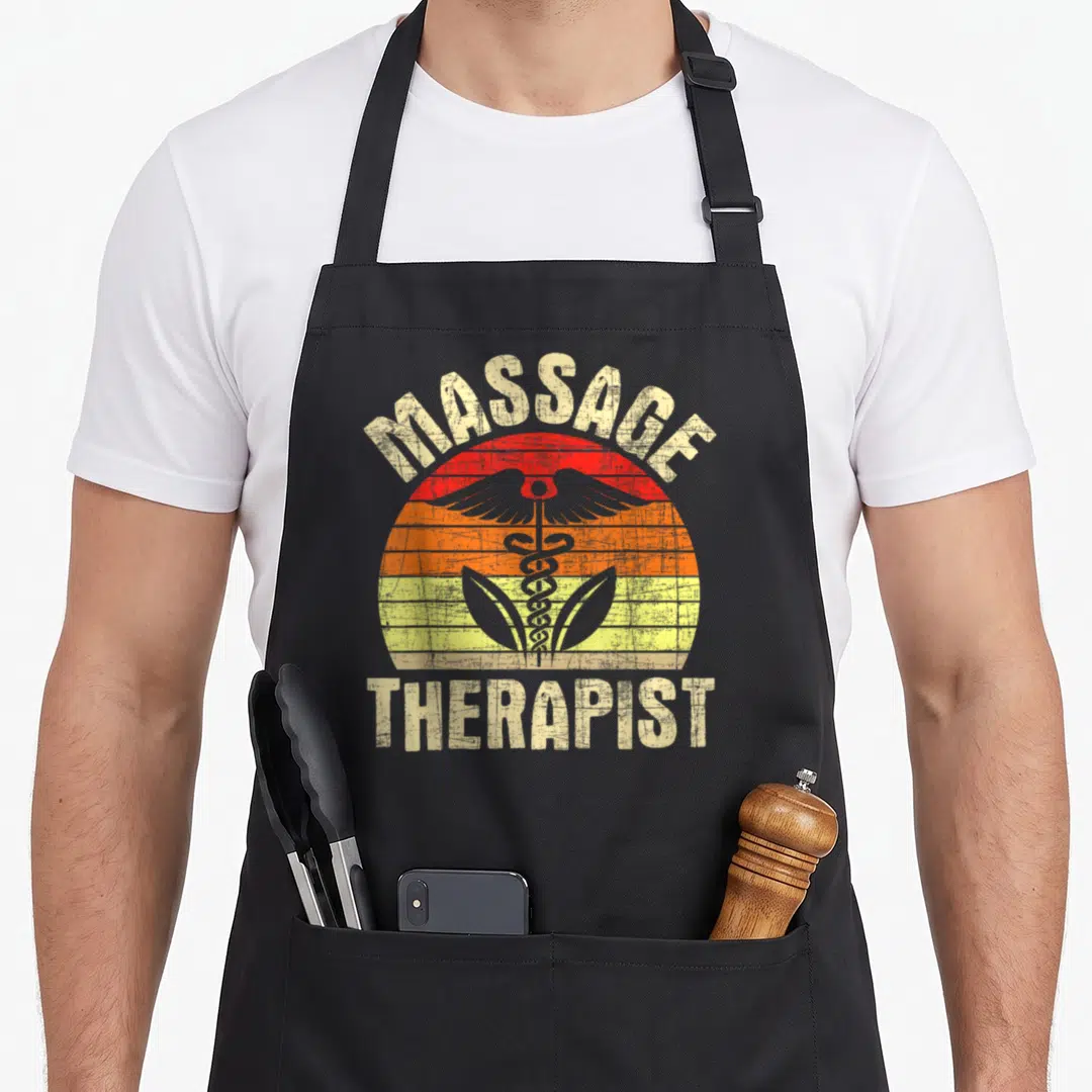 Massotherapist massage therapist apron - MASSAGE THERAPIST text around a striped sun with a grey caduceus in red orange — shown on a black cotton canvas apron against a white background