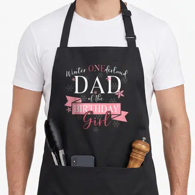 Onederland birthday winter apron - Stacked text Winter ONEderland DAD of the BIRTHDAY Girl with pink ribbon — shown on a black cotton canvas apron against a white background