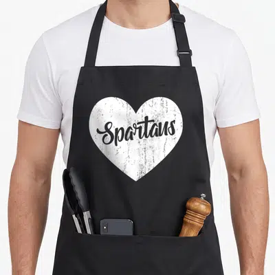 Spartan novelty apron - White distressed heart containing grey cursive Spartans text — shown on a black cotton canvas apron against a white background