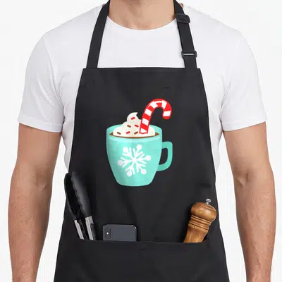 Hot candy cane apron - Light blue mug with hot chocolate, whipped cream, striped candy cane, and snowflake — shown on a black cotton canvas apron against a white background