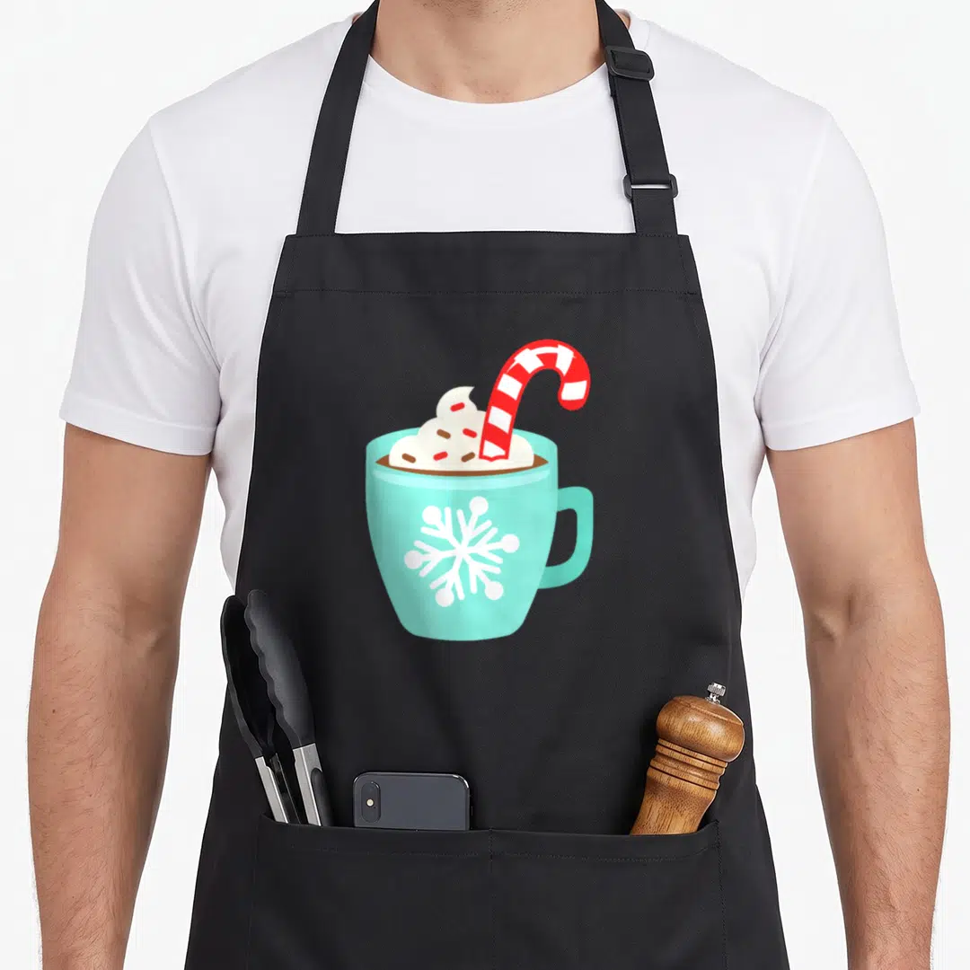 Hot candy cane apron - Light blue mug with hot chocolate, whipped cream, striped candy cane, and snowflake — shown on a black cotton canvas apron against a white background