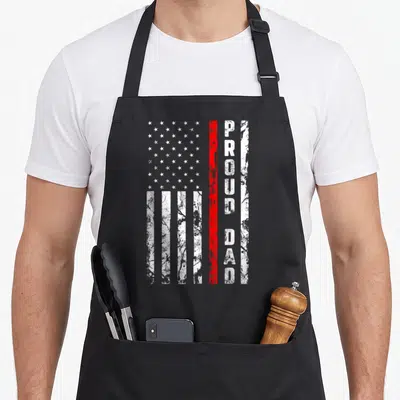 Patriotic firefighter aprons - Vertical PROUD DAD text beside distressed flag with red stripe and white stars — shown on a black cotton canvas apron against a white background