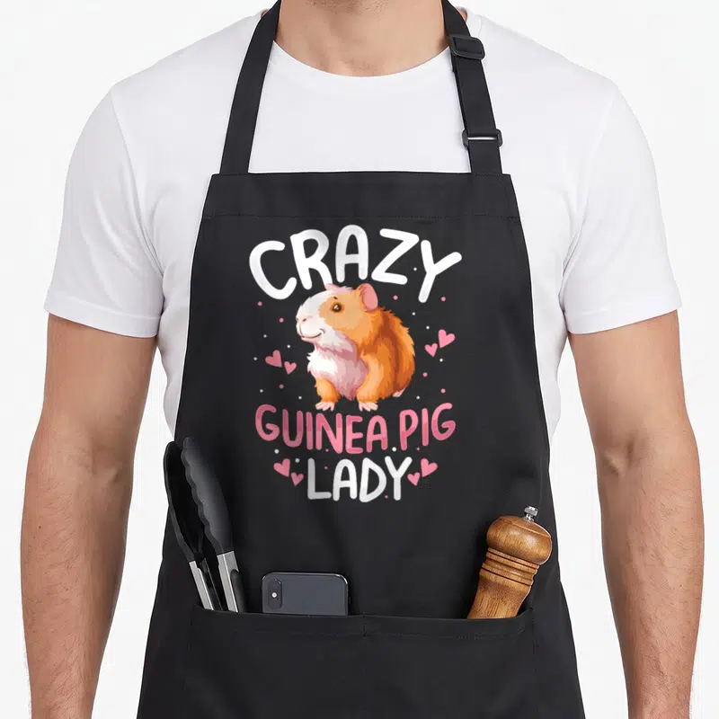 Vintage pig animal crazy guinea lady apron - Cartoon guinea pig in orange and white with hearts and dots under arched — shown on a black cotton canvas apron against a white background