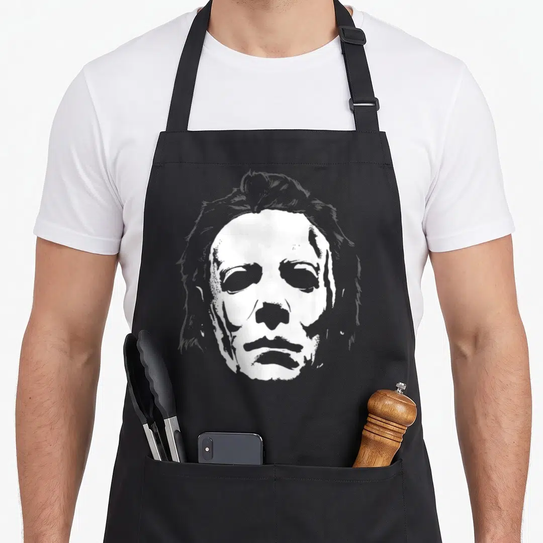 Mask halloween apron - White line-art illustration of a masked face centered on a black background — shown on a black cotton canvas apron against a white background