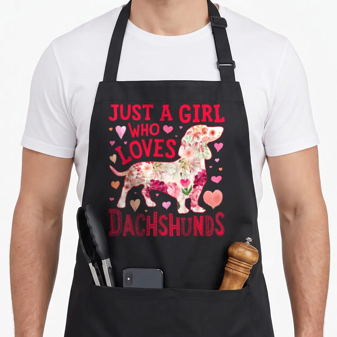 Flower dachshund apron - Just A Girl Who Loves Dachshunds text surrounding a floral-filled dachshund silhouette — shown on a black cotton canvas apron against a white background