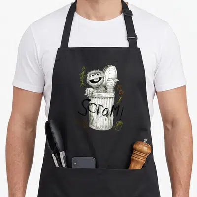 Scram oscar the grouch apron - Oscar the Grouch in trash can with Scram text and scattered fish bones and sneakers — shown on a black cotton canvas apron against a white background