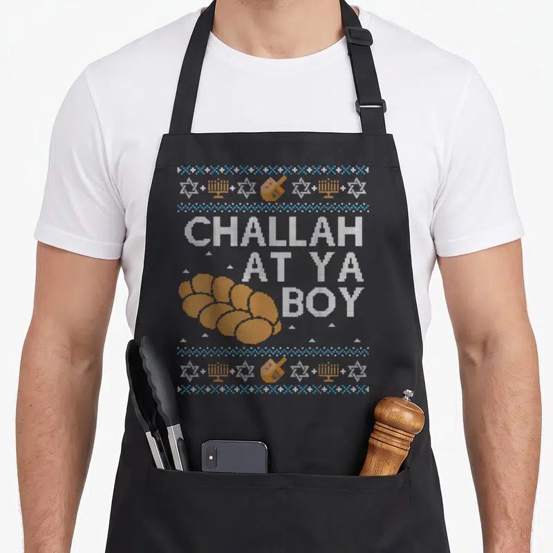 Ugly hanukkah apron - Orange challah bread next to white text CHALLAH AT YA BOY with blue and white borders containing — shown on a black cotton canvas apron against a white background