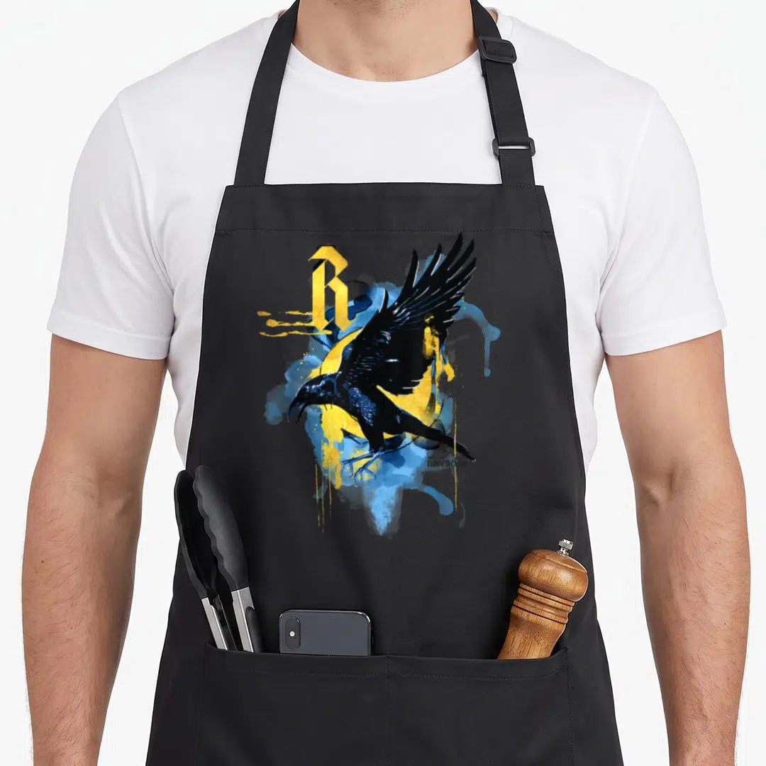 Elegance urban apron - Black raven, yellow R, blue splashes, ravenclaw text — shown on a black cotton canvas apron against a white background