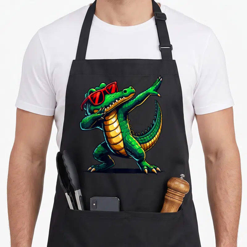 Crocodile animal apron - Green cartoon crocodile dabbing with red sunglasses on black apron — shown on a black cotton canvas apron against a white background