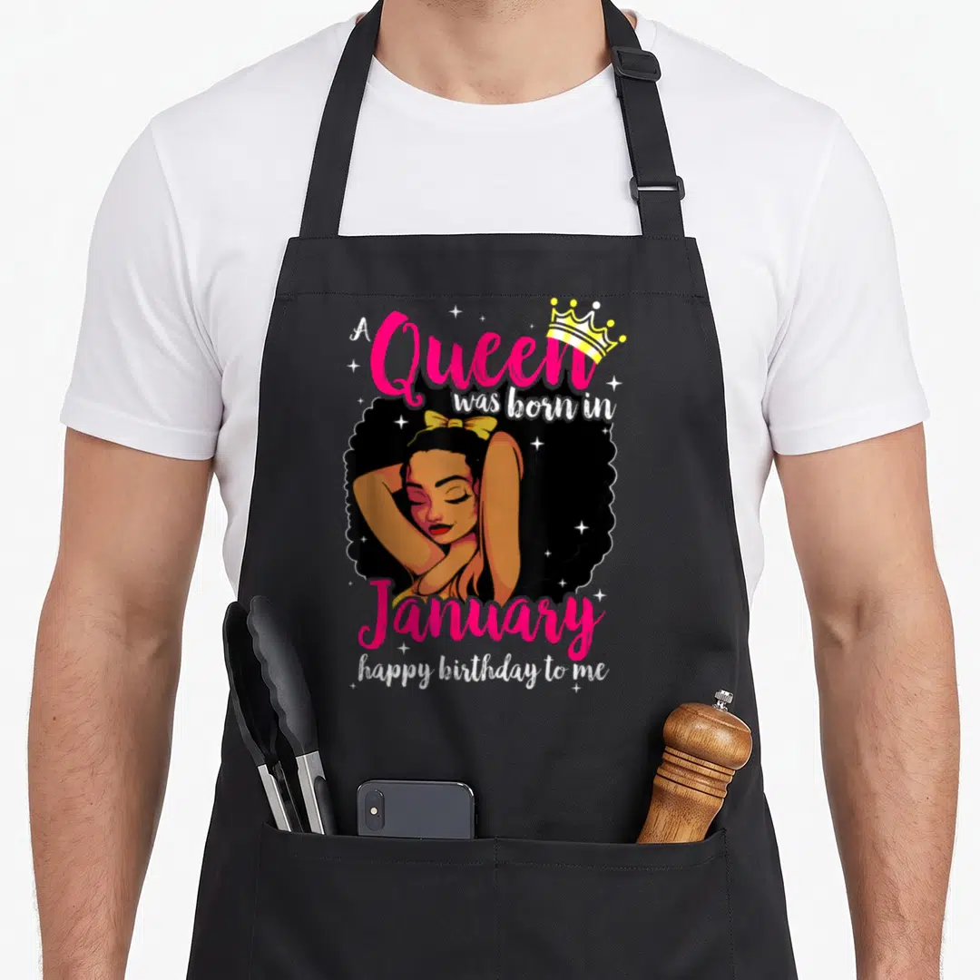 Diva queen birthday apron - Cartoon woman with crown and A Queen was born in January text in pink and gold — shown on a black cotton canvas apron against a white background