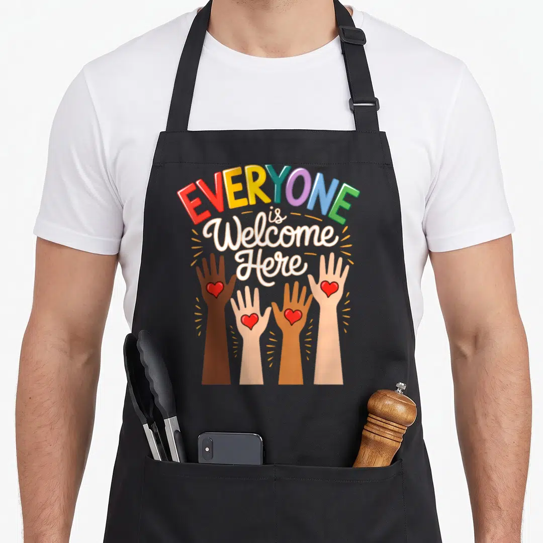 Welcome idaho teacher apron - Four diverse hands with red hearts reaching up under rainbow text reading EVERYONE is — shown on a black cotton canvas apron against a white background