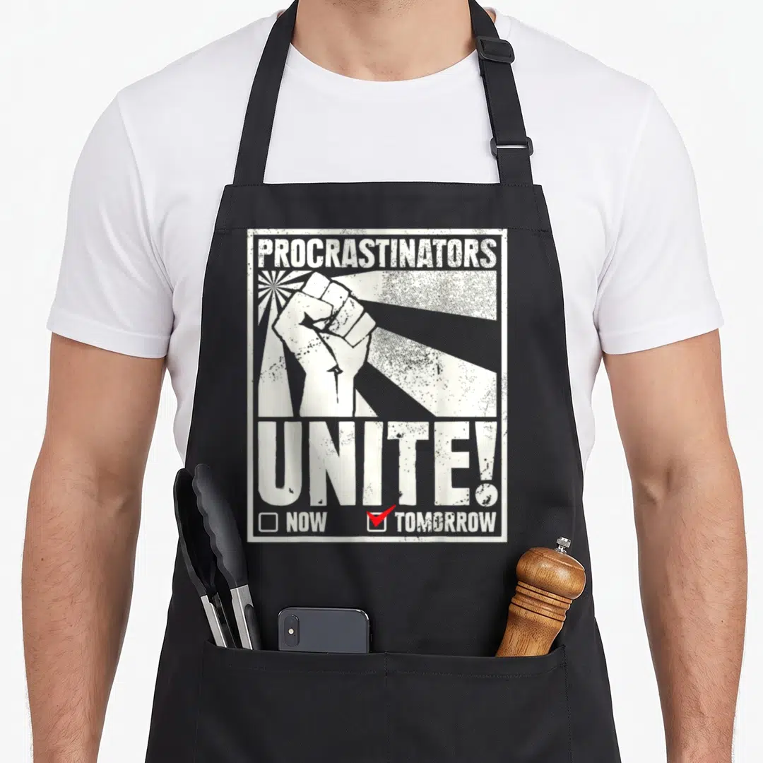Cute unite procrastinator apron - Distressed fist with sunburst and checkboxes for Now and Tomorrow in white and red — shown on a black cotton canvas apron against a white background