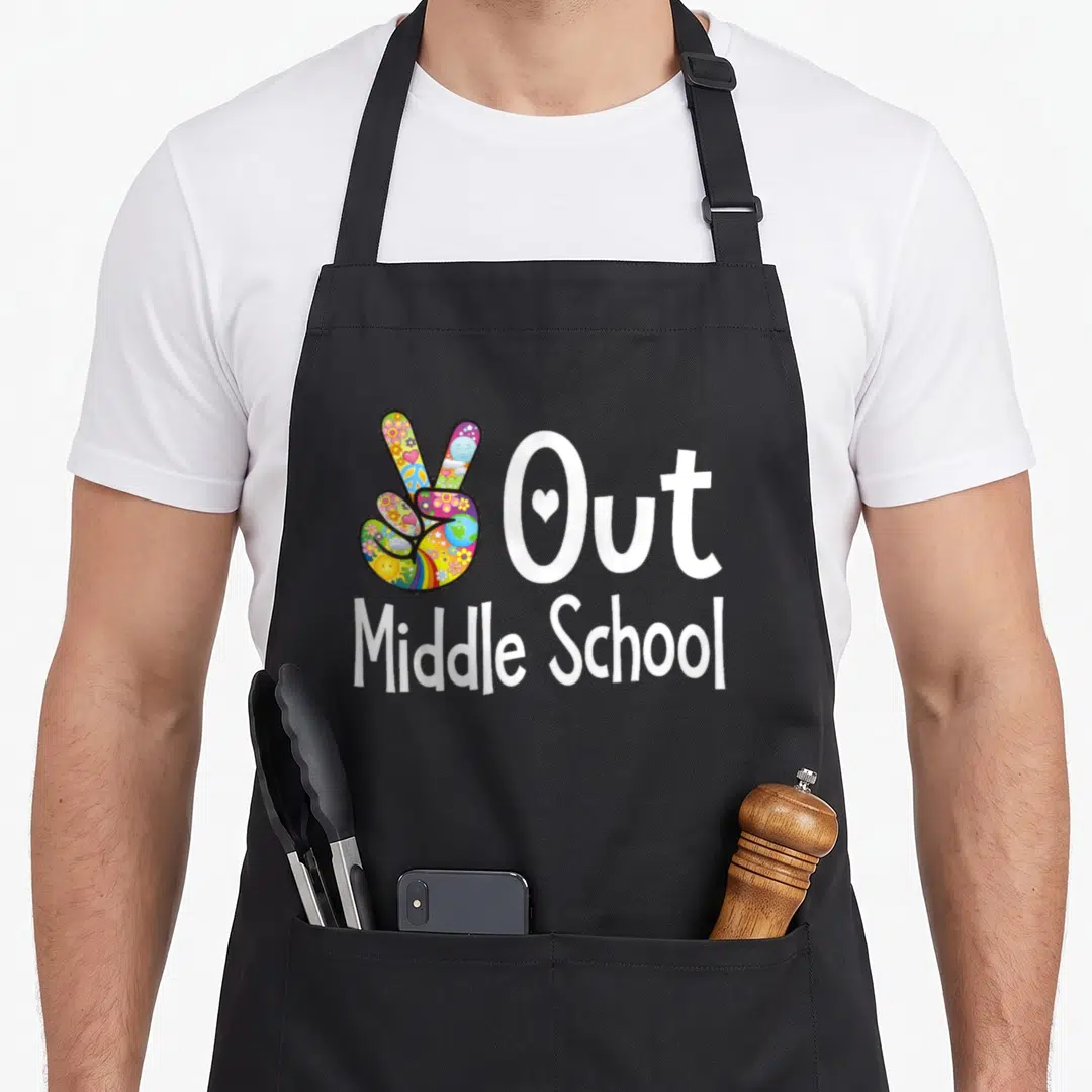 Peace middle child apron - Multicolored peace sign hand next to white Out Middle School text with heart in O — shown on a black cotton canvas apron against a white background
