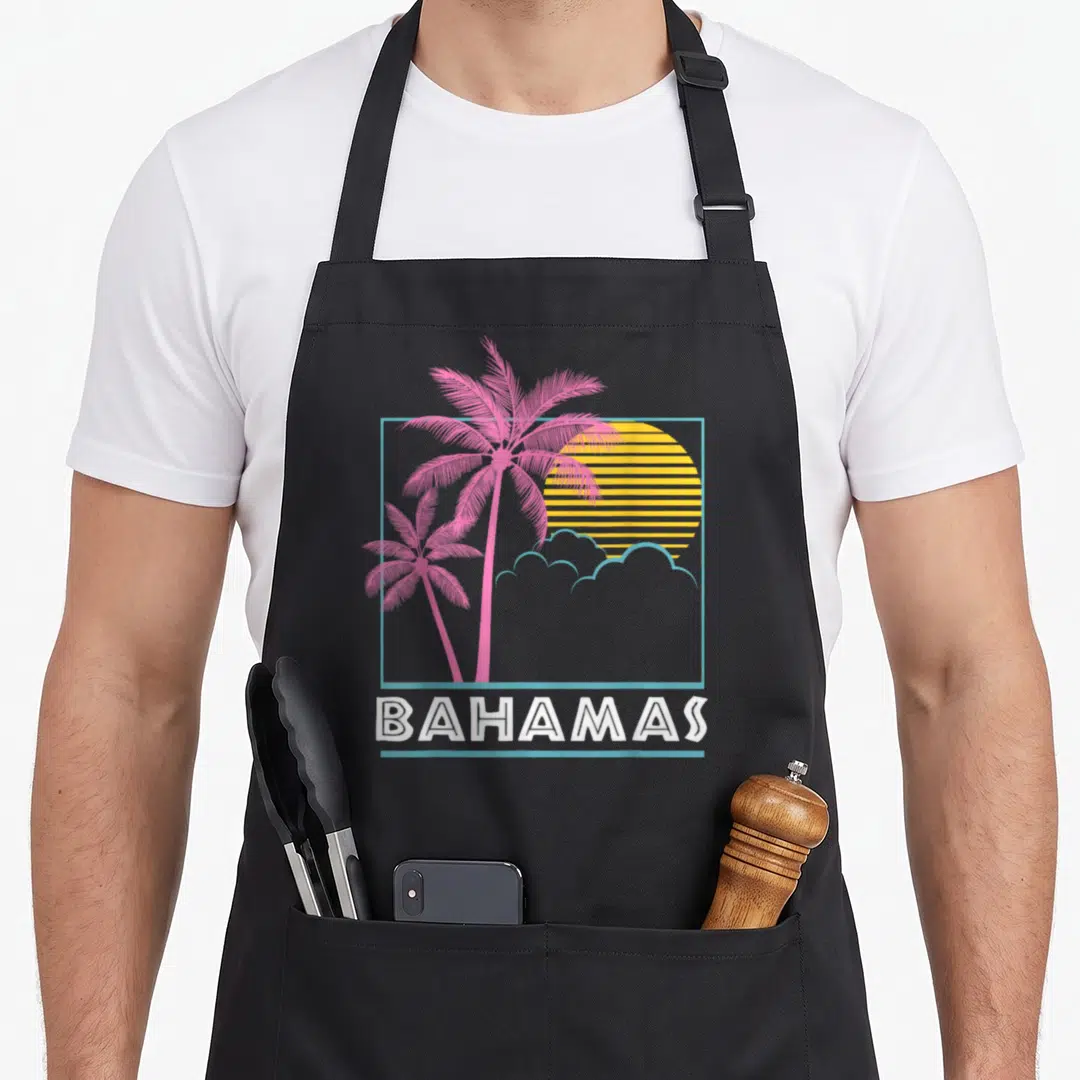 Flag bahamian apron - Retro pink palm trees over yellow striped sun with BAHAMAS text in white — shown on a black cotton canvas apron against a white background