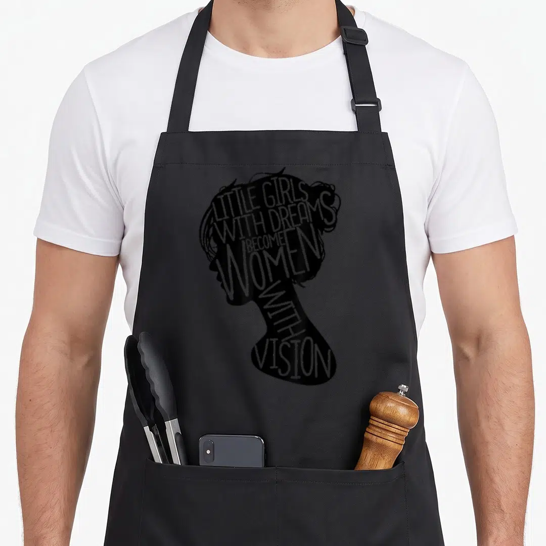 Feminist social apron - Black silhouette of a woman's head from the side formed by text reading LITTLE GIRLS — shown on a black cotton canvas apron against a white background