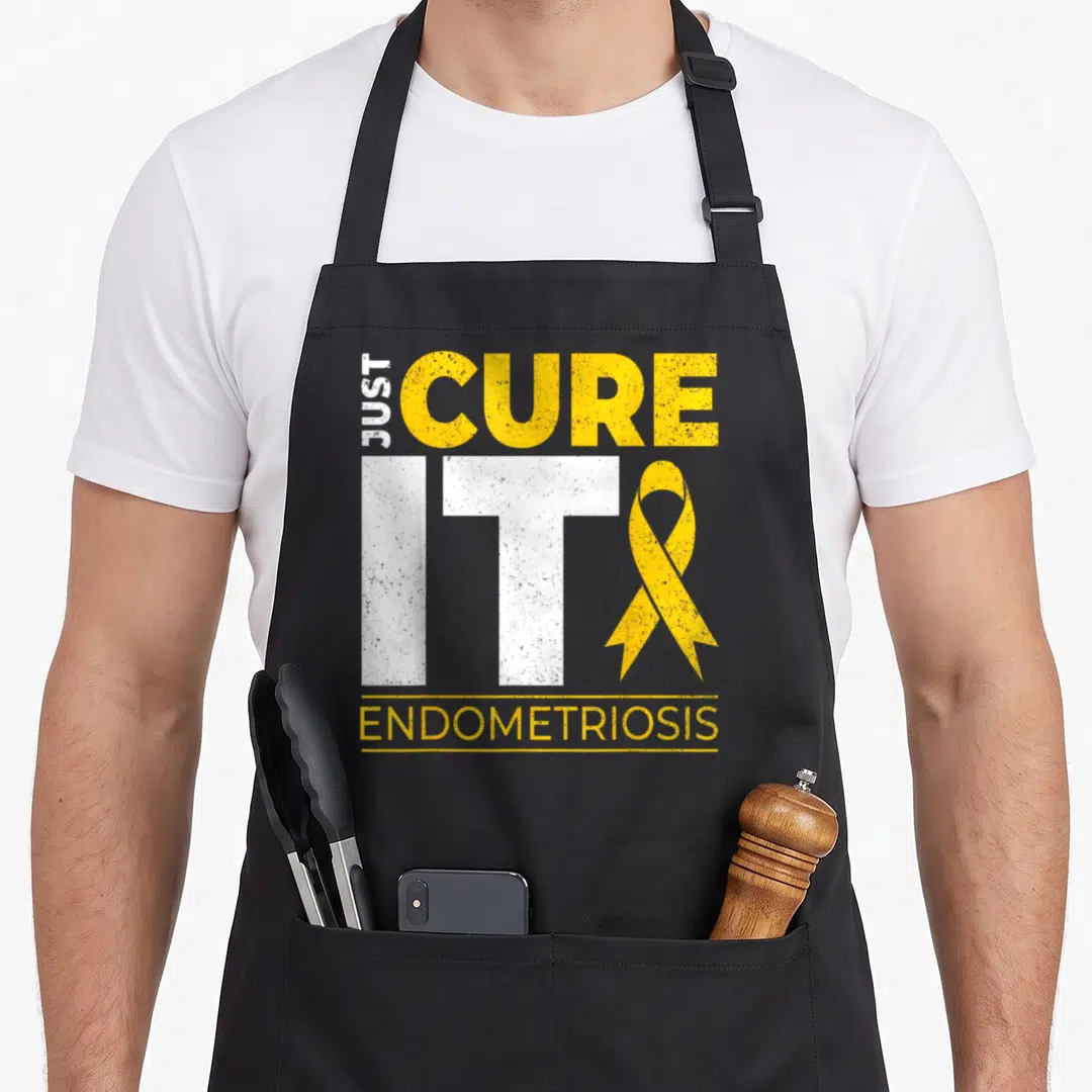 Cure endometriosis ribbon apron - Just Cure It Endometriosis text with yellow ribbon and white letters — shown on a black cotton canvas apron against a white background