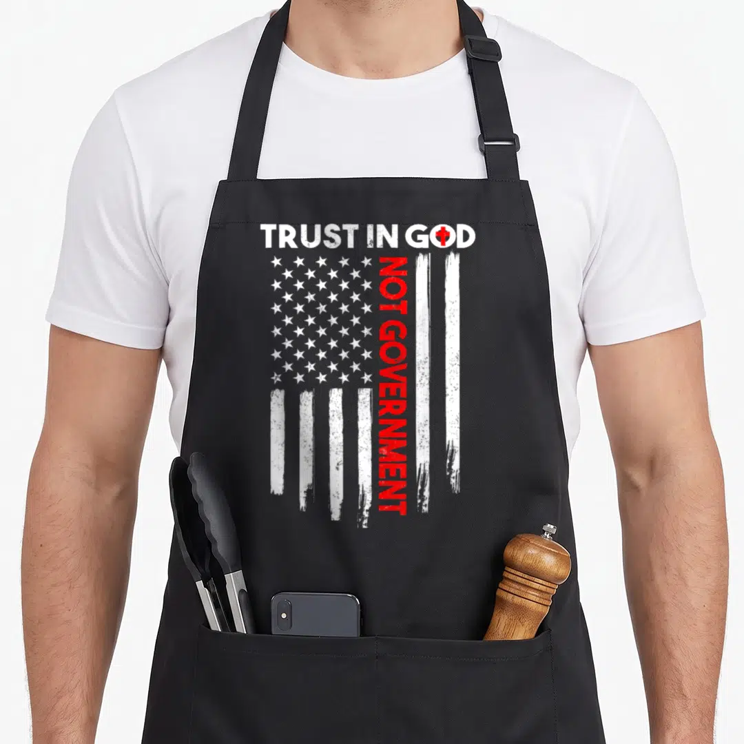 Government patriotic apron - Distressed US flag with vertical red text NOT GOVERNMENT under white TRUST IN GOD header — shown on a black cotton canvas apron against a white background