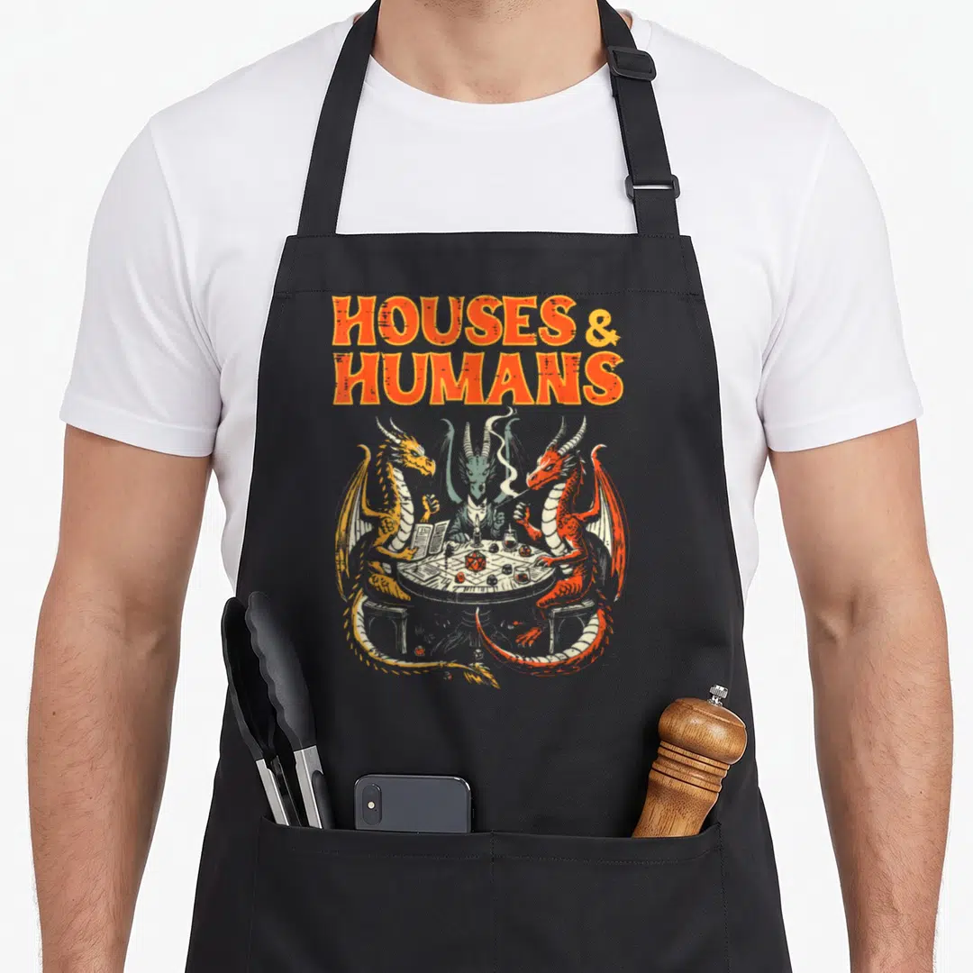 Human gaming apron - Three dragons playing dice under stacked Houses & Humans text in orange yellow green red grey — shown on a black cotton canvas apron against a white background
