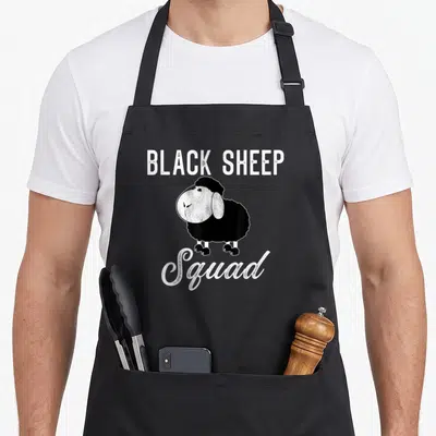 Squad sheep apron - Cartoon black sheep with BLACK SHEEP Squad text in white lettering — shown on a black cotton canvas apron against a white background
