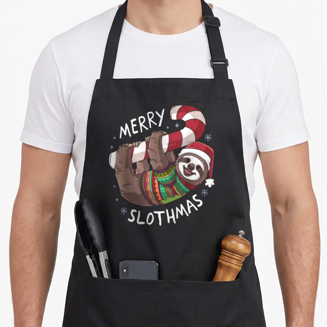 Sloth womens christmas aprons - Cartoon sloth hanging from red and white candy cane wearing sweater and Santa hat — shown on a black cotton canvas apron against a white background