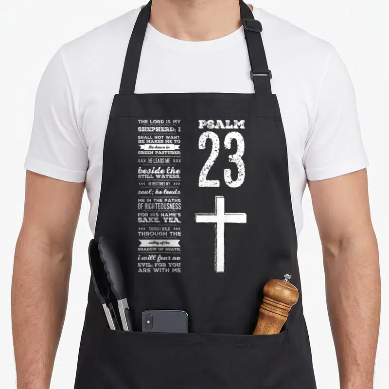 Youth christian apron - Psalm 23 text stacked left, large 23 and cross right, white distressed print — shown on a black cotton canvas apron against a white background