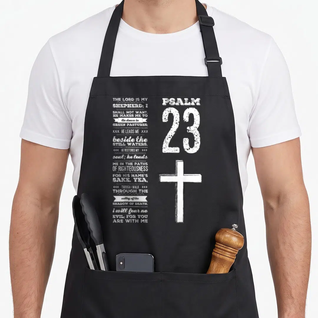 Youth christian apron - Psalm 23 text stacked left, large 23 and cross right, white distressed print — shown on a black cotton canvas apron against a white background