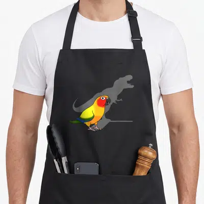 Parrot meme apron - Cartoon parrot with yellow red blue green feathers casting grey T-Rex shadow — shown on a black cotton canvas apron against a white background