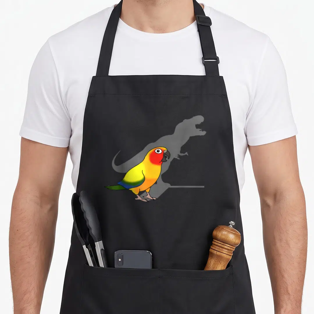 Parrot meme apron - Cartoon parrot with yellow red blue green feathers casting grey T-Rex shadow — shown on a black cotton canvas apron against a white background