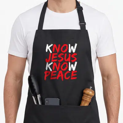 Jesus bible verse apron - Stacked KNOW JESUS KNOW PEACE text in white and red brush stroke font — shown on a black cotton canvas apron against a white background