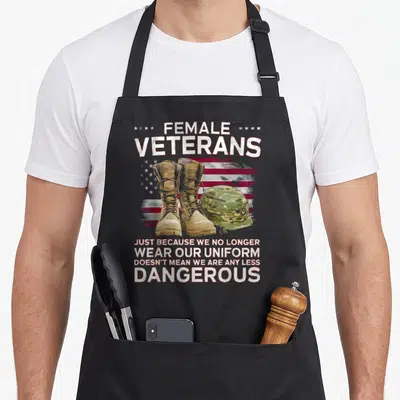 Veteran uniform apron - FEMALE VETERANS text above tan boots and camo helmet on distressed flag background — shown on a black cotton canvas apron against a white background