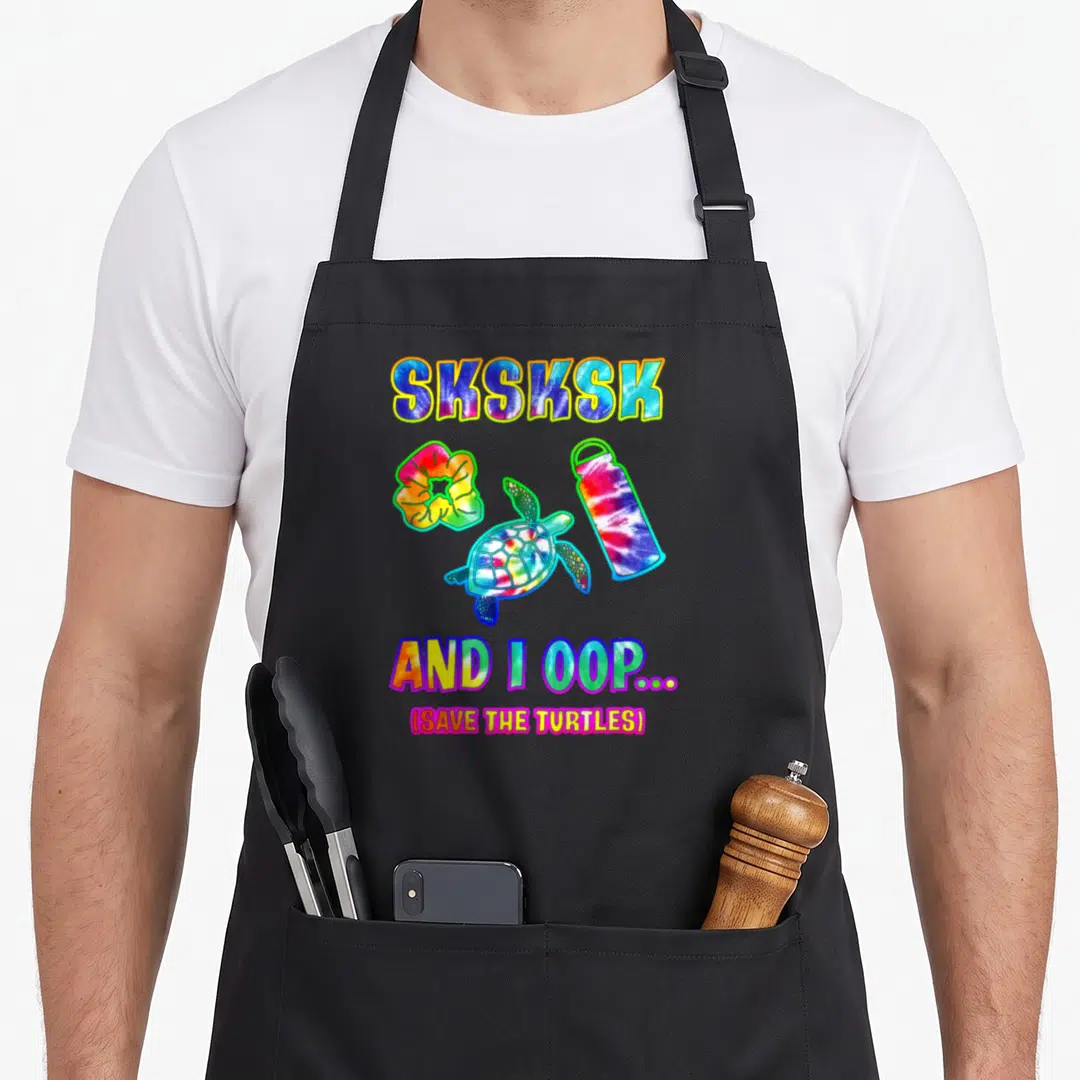Sksksk tie dye apron - Cartoon turtle, scrunchie, and bottle in tie dye colors with sksksk text — shown on a black cotton canvas apron against a white background