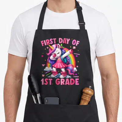 Outfit unicorn apron - Dabbing unicorn with FIRST DAY OF 1ST GRADE text and rainbow in pink purple blue yellow — shown on a black cotton canvas apron against a white background
