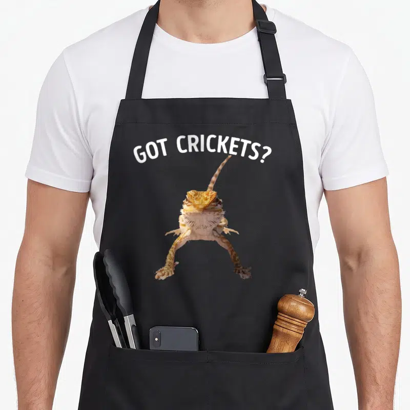 Bearded cricket apron - Arched GOT CRICKETS? text above orange tan white bearded dragon photo on black bib — shown on a black cotton canvas apron against a white background