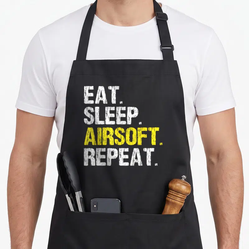 Repeat airsoft apron - Stacked white and yellow distressed text reading EAT. SLEEP. AIRSOFT. REPEAT — shown on a black cotton canvas apron against a white background
