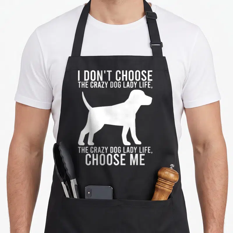 Chose dog cooking apron - White dog silhouette between text blocks reading I don't choose the crazy dog lady life — shown on a black cotton canvas apron against a white background