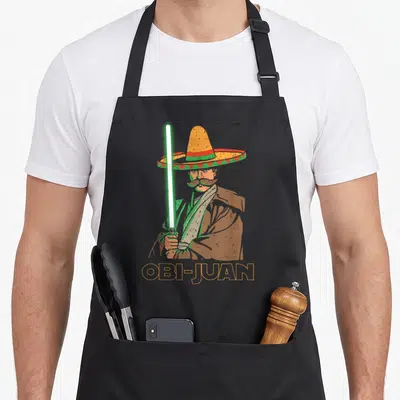 Obi mexican apron - Retro man in sombrero holding green lightsaber above orange OBI-JUAN text outline — shown on a black cotton canvas apron against a white background