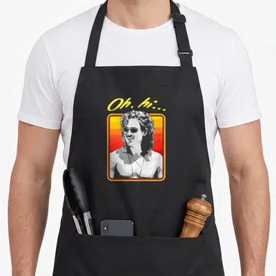 Greyscale billy apron - Oh hi text above man portrait in yellow frame with red gradient background — shown on a black cotton canvas apron against a white background