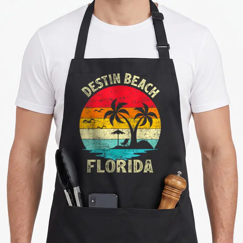 Vacation florida family aprons - Retro Destin Beach Florida sunset with palm trees, beach chair, and multi-colored bands — shown on a black cotton canvas apron against a white background