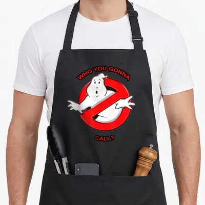 Call novelty apron - Red prohibition sign with white cartoon ghost and arched WHO YOU GONNA CALL text — shown on a black cotton canvas apron against a white background