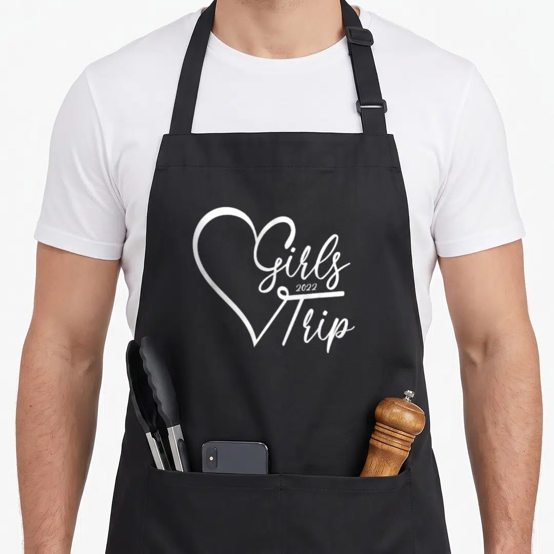 Funny trip girls weekend apron - White heart outline overlapping Girls Trip 2022 script text — shown on a black cotton canvas apron against a white background