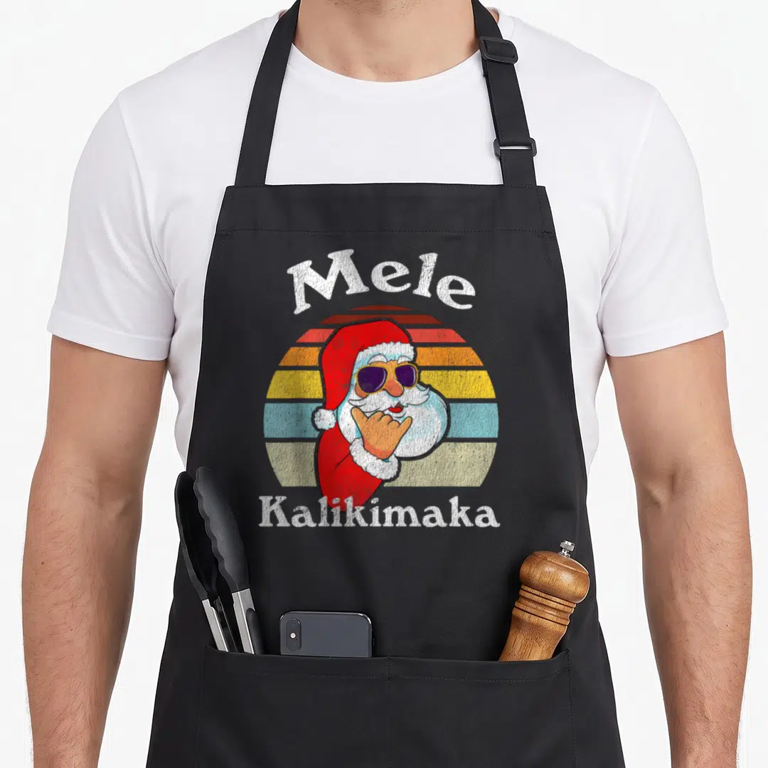 Kalikimaka christmas santa apron - Mele Kalikimaka text above Santa with sunglasses in front of striped sun background — shown on a black cotton canvas apron against a white background