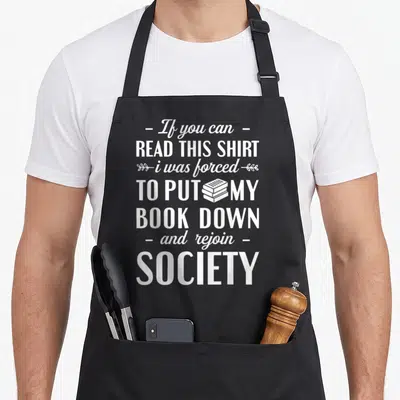 Bookworm book lovers apron - White vertical typography reading If you can read this shirt i was forced to put my book — shown on a black cotton canvas apron against a white background
