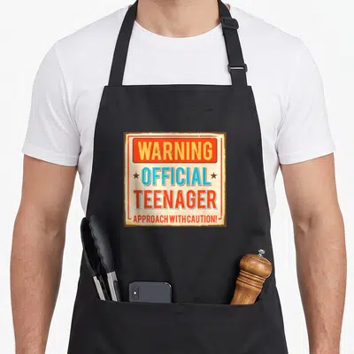 Warning ideas apron - Distressed red and beige typographic sign reading WARNING OFFICIAL TEENAGER APPROACH WITH CAUTION — shown on a black cotton canvas apron against a white background