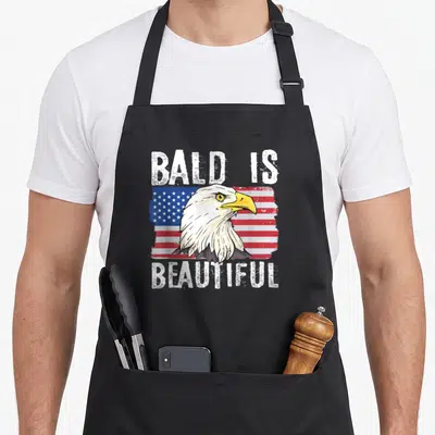 Beautiful 4th of july apron - Bald eagle head over distressed red white and blue flag with BALD IS BEAUTIFUL text — shown on a black cotton canvas apron against a white background