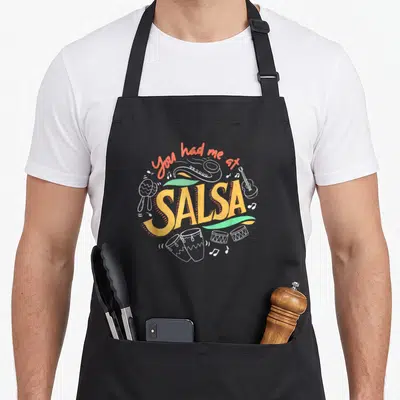 Dancing ballroom apron - You had me at SALSA text with maracas guitar drums and green ribbons in orange white and green — shown on a black cotton canvas apron against a white background