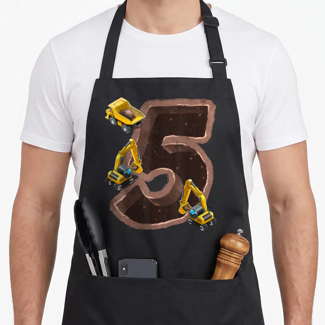 5th birthday vehicle apron - Cartoon number 5 excavation hole with yellow dump truck and two excavators on brown dirt — shown on a black cotton canvas apron against a white background